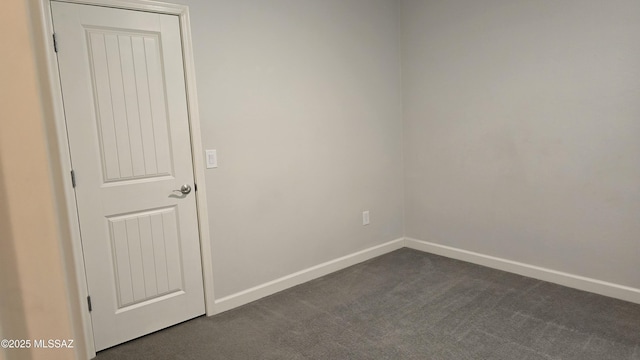 spare room featuring dark colored carpet and baseboards