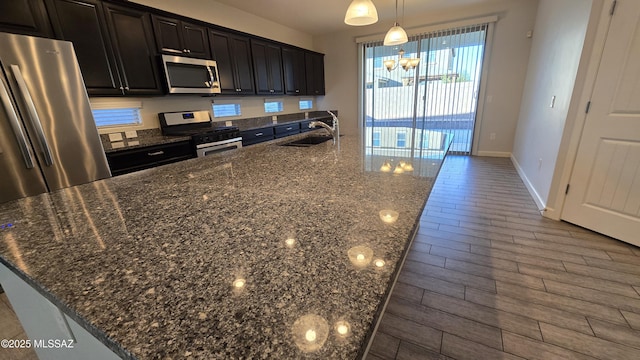 kitchen with baseboards, a sink, a chandelier, stainless steel appliances, and a large island with sink