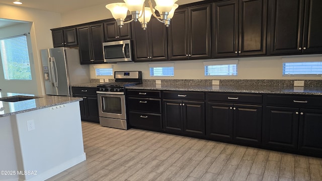 kitchen with a notable chandelier, a sink, light wood-style flooring, and appliances with stainless steel finishes