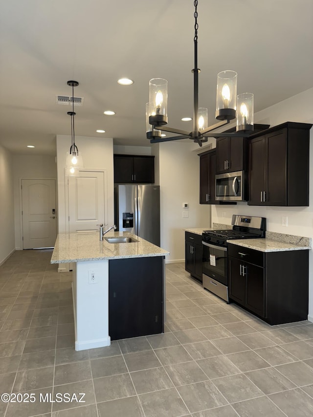 kitchen with sink, pendant lighting, stainless steel appliances, an island with sink, and light stone countertops