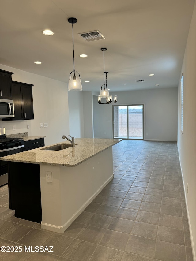 kitchen with a center island with sink, stainless steel appliances, light stone counters, decorative light fixtures, and sink