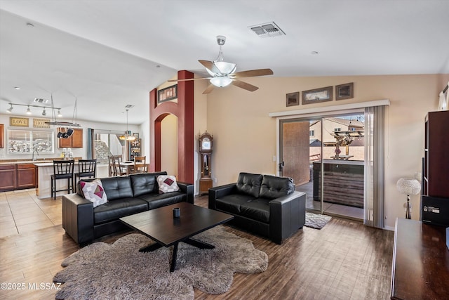 living room featuring arched walkways, wood finished floors, lofted ceiling, and visible vents