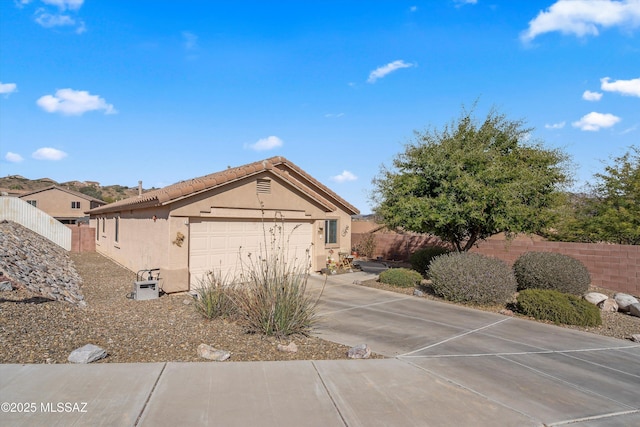 exterior space featuring a garage, a tile roof, fence, concrete driveway, and stucco siding