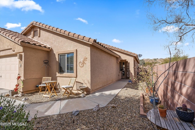 view of side of property featuring a tile roof, fence, an attached garage, and stucco siding