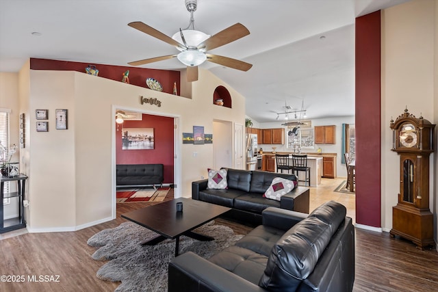 living room featuring ceiling fan, light wood-style flooring, baseboards, and vaulted ceiling