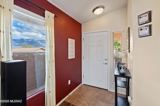 entrance foyer with vaulted ceiling, light tile patterned flooring, a mountain view, and baseboards