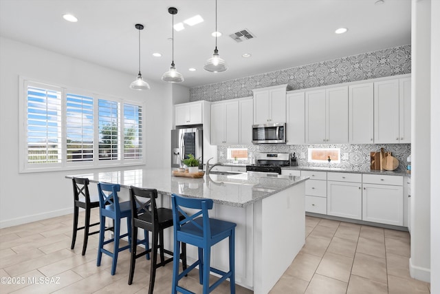 kitchen featuring tasteful backsplash, an island with sink, stainless steel appliances, white cabinets, and visible vents