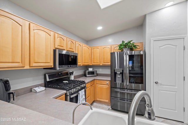 kitchen featuring light countertops, appliances with stainless steel finishes, a sink, and light brown cabinetry