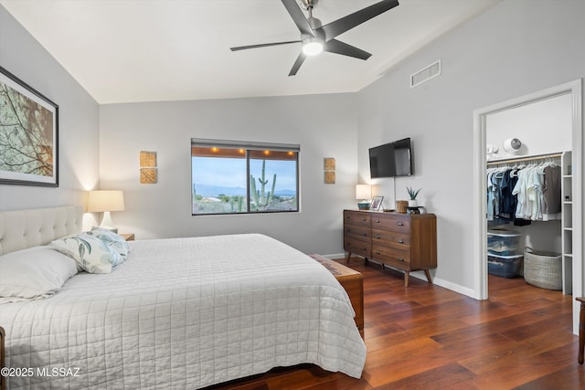 bedroom featuring visible vents, baseboards, a walk in closet, wood finished floors, and vaulted ceiling