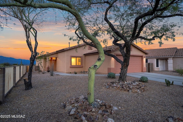 view of front of home featuring a garage, a tile roof, fence, stucco siding, and driveway