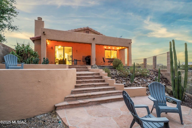 back of property at dusk featuring a patio, fence private yard, and stucco siding