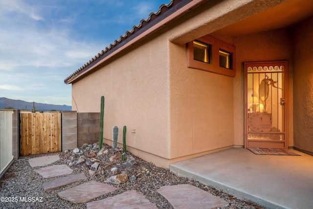 view of side of home with a mountain view, stucco siding, and fence