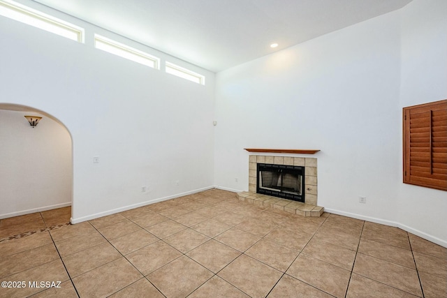 unfurnished living room featuring a tile fireplace, light tile patterned floors, baseboards, arched walkways, and recessed lighting