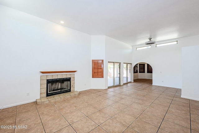 unfurnished living room featuring a towering ceiling, baseboards, a tile fireplace, and light tile patterned floors
