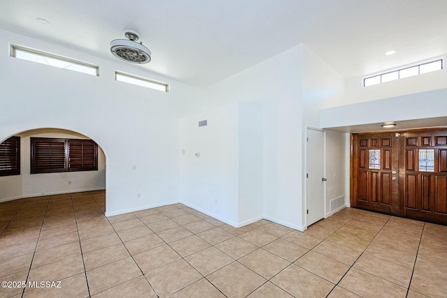 empty room with baseboards, visible vents, a high ceiling, and light tile patterned floors