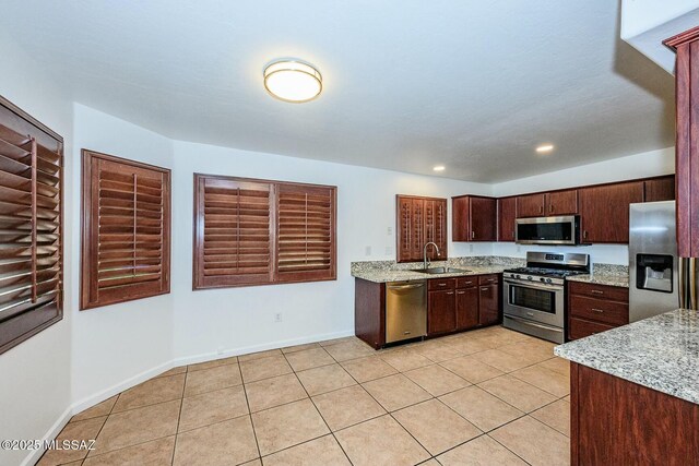 kitchen with light tile patterned floors, a sink, stainless steel appliances, and baseboards