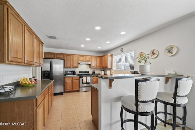 kitchen with light tile patterned flooring, a kitchen bar, stainless steel appliances, and a textured ceiling