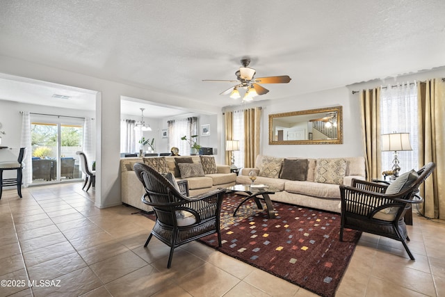 tiled living room featuring a textured ceiling and ceiling fan with notable chandelier