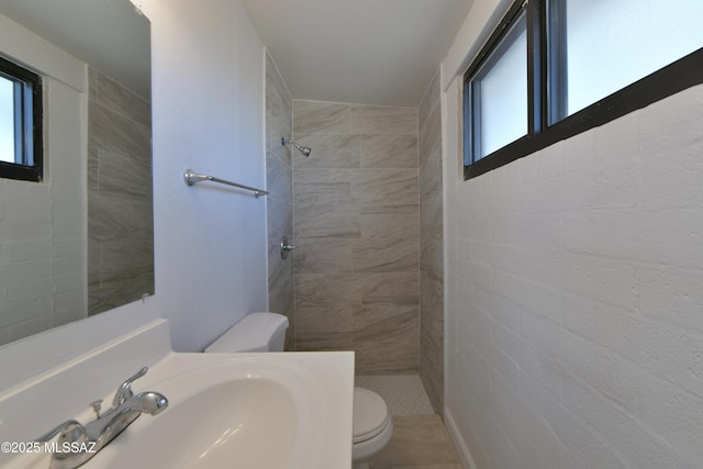 bathroom featuring tiled shower, a sink, and toilet