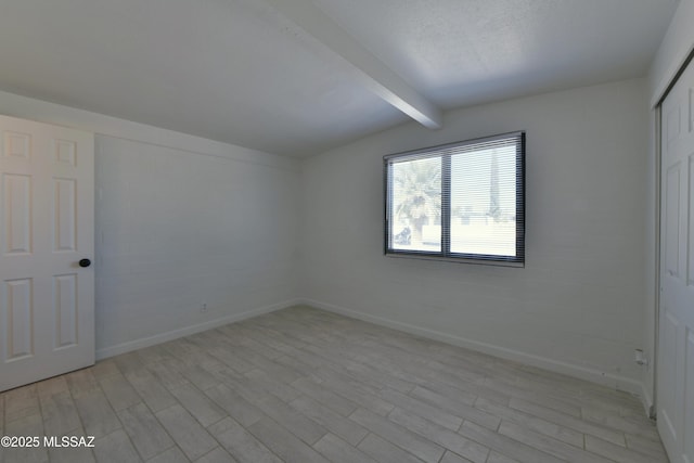 additional living space featuring lofted ceiling with beams, light wood-style flooring, baseboards, and a textured ceiling