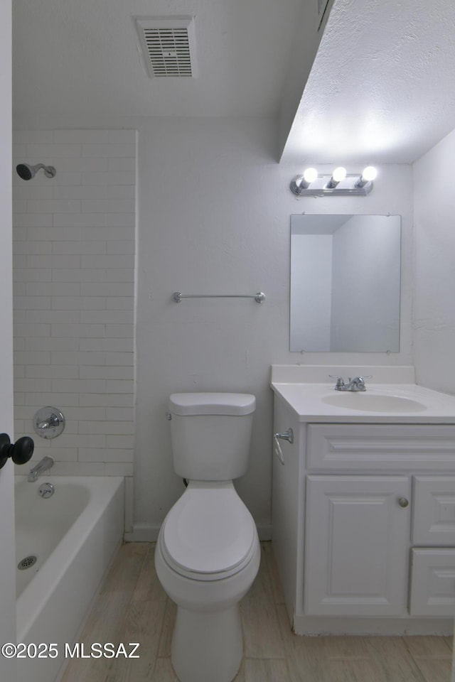 bathroom featuring visible vents, toilet, vanity, wood finished floors, and shower / bathtub combination