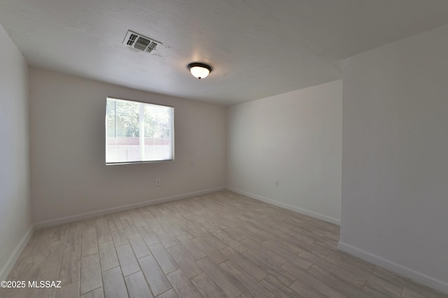 spare room with light wood-type flooring, visible vents, a textured ceiling, and baseboards