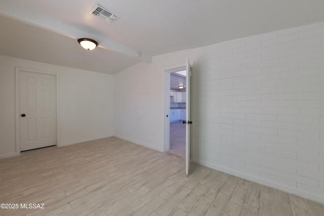 empty room featuring lofted ceiling, brick wall, visible vents, and light wood-style floors