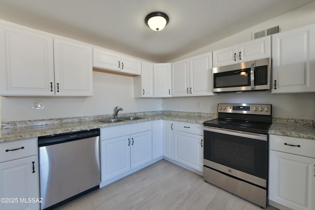 kitchen with stainless steel appliances, lofted ceiling, light wood-style floors, white cabinets, and a sink