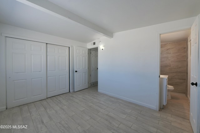 unfurnished bedroom with beamed ceiling, a closet, visible vents, and wood tiled floor