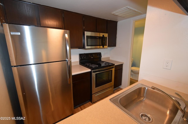 kitchen with sink, stainless steel appliances, dark brown cabinetry, and light hardwood / wood-style flooring