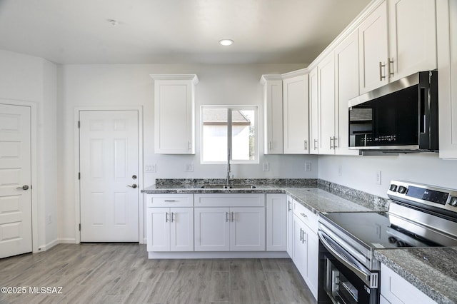 kitchen featuring dark stone countertops, sink, white cabinetry, light hardwood / wood-style floors, and stainless steel electric stove