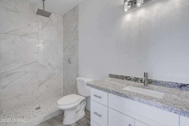 bathroom featuring toilet, tiled shower, and vanity