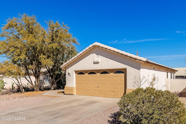 view of side of home featuring concrete driveway, a tiled roof, an attached garage, and stucco siding