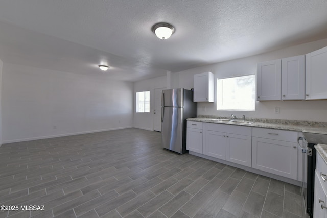 kitchen featuring a sink, a textured ceiling, open floor plan, stainless steel appliances, and baseboards