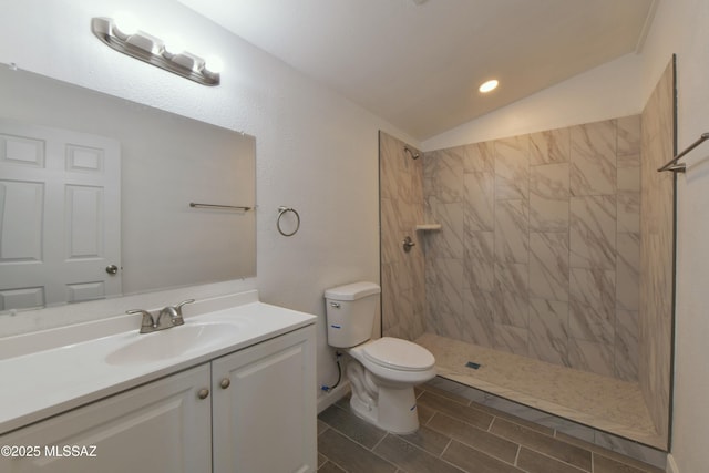 bathroom featuring tiled shower, toilet, vanity, and vaulted ceiling