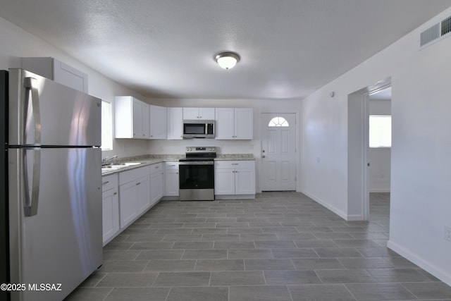 kitchen with baseboards, visible vents, a sink, appliances with stainless steel finishes, and white cabinetry