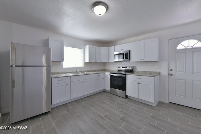 kitchen featuring a sink, a textured ceiling, appliances with stainless steel finishes, white cabinets, and light stone countertops