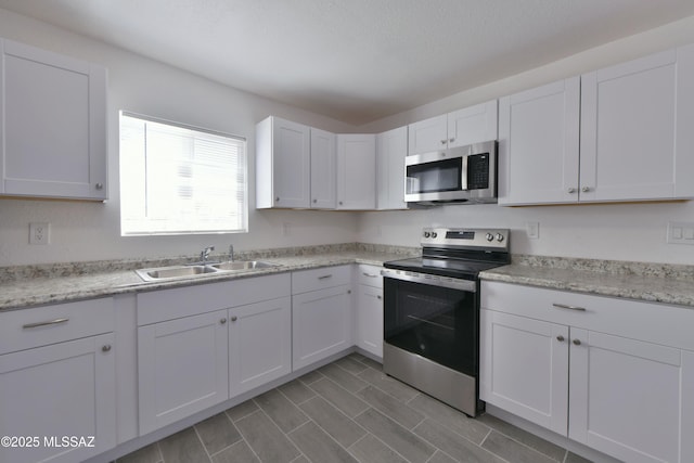 kitchen with white cabinetry, stainless steel appliances, light countertops, and a sink