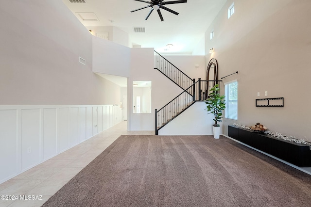 unfurnished living room with light carpet, ceiling fan, and a towering ceiling