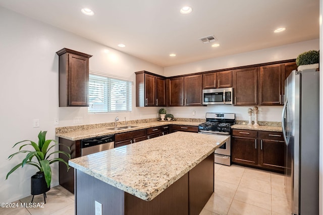 kitchen featuring appliances with stainless steel finishes, dark brown cabinets, light stone countertops, a kitchen island, and sink