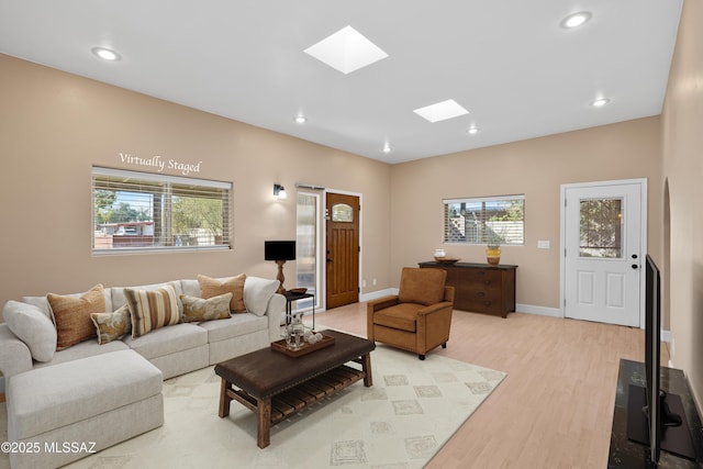 living room with a healthy amount of sunlight, a skylight, baseboards, and light wood-style floors