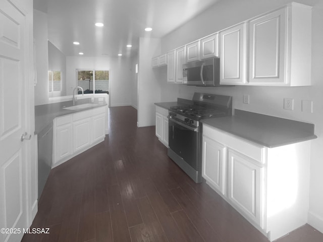 kitchen with white cabinets, dark countertops, dark wood-style floors, stainless steel appliances, and a sink