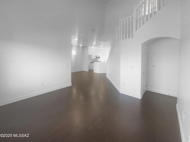 interior space featuring stairs, a high ceiling, baseboards, and dark wood-style flooring