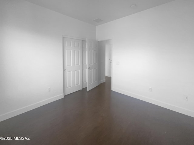 unfurnished room with dark wood-style floors, visible vents, and baseboards