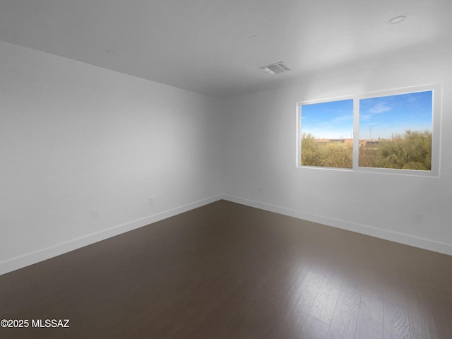 spare room with wood finished floors, visible vents, and baseboards