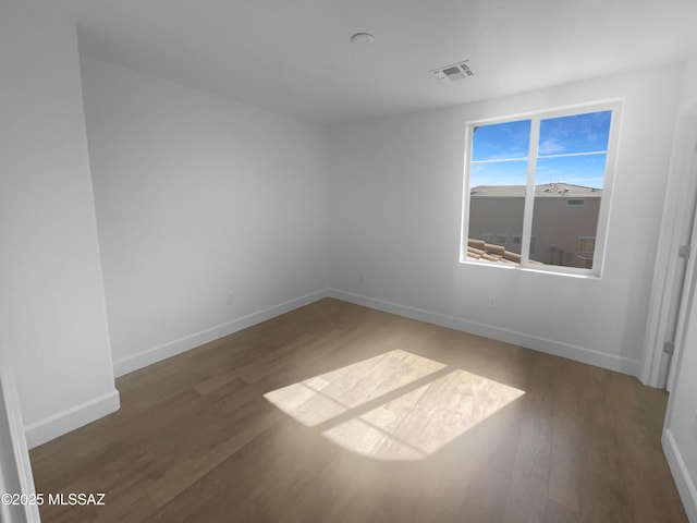 spare room featuring visible vents, dark wood finished floors, and baseboards