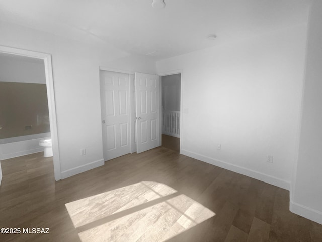 unfurnished bedroom featuring ensuite bath, a closet, baseboards, and dark wood-type flooring