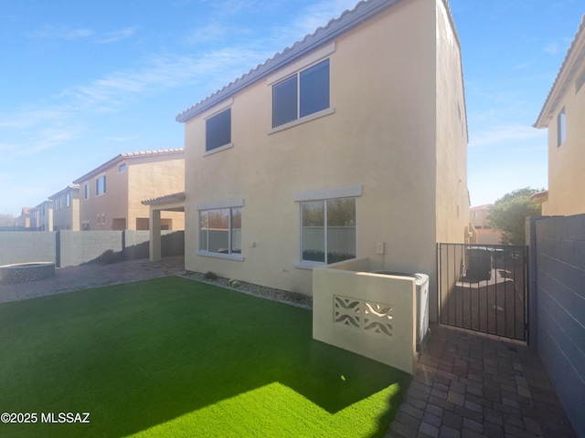 rear view of property with fence, a tiled roof, a lawn, a gate, and stucco siding