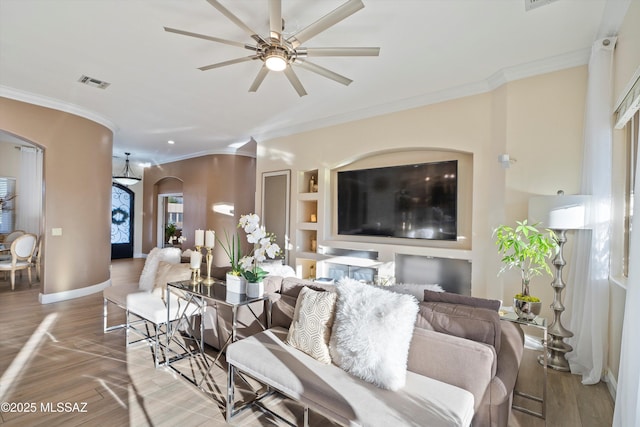 living area with wood finished floors, visible vents, a ceiling fan, arched walkways, and crown molding