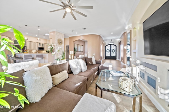 living area with a ceiling fan, arched walkways, light wood-style floors, and crown molding
